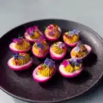 Colorful pink deviled eggs garnished with herbs.