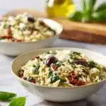 A colorful orzo pasta salad with feta cheese and sun-dried tomatoes